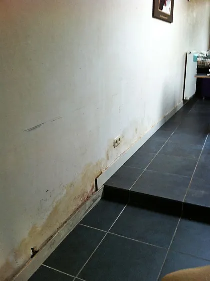Vochtschade en afbladderende pleister onderaan een binnenmuur door opstijgend vocht